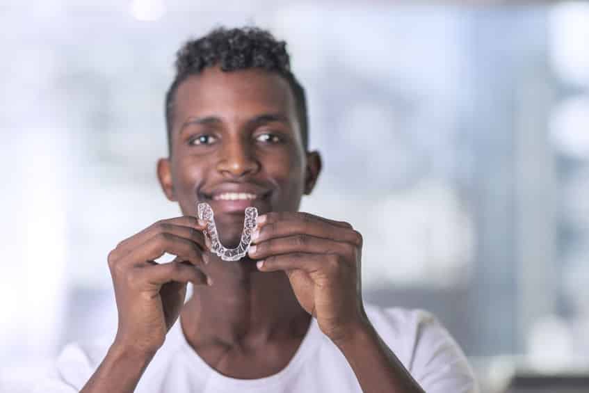 A man holding up a clear aligner with two hands.