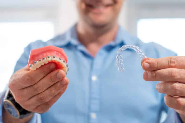 dentist holding invisalign on one hand and teeth model with braces on the other