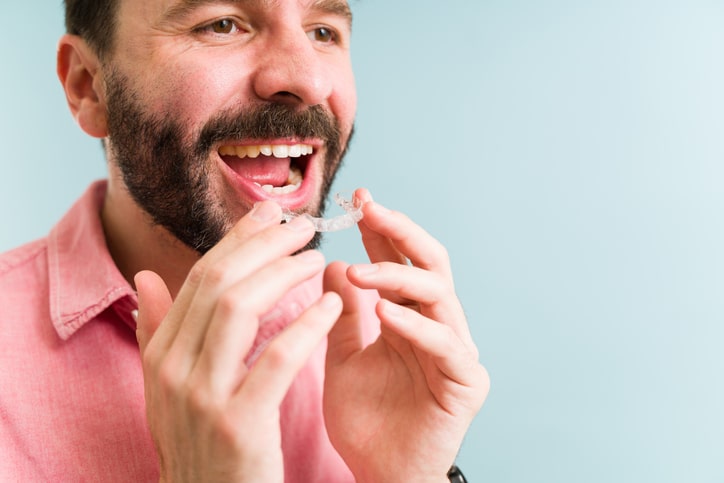 A bearded man in a pink shirt about to apply his clear aligners.