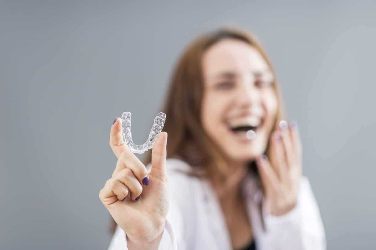 a person smiling while displaying invisalign clear aligners with her fingers