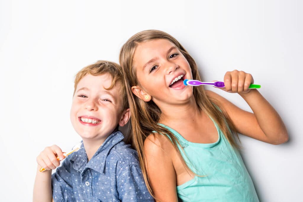 two children smiling while holding their own toothbrush