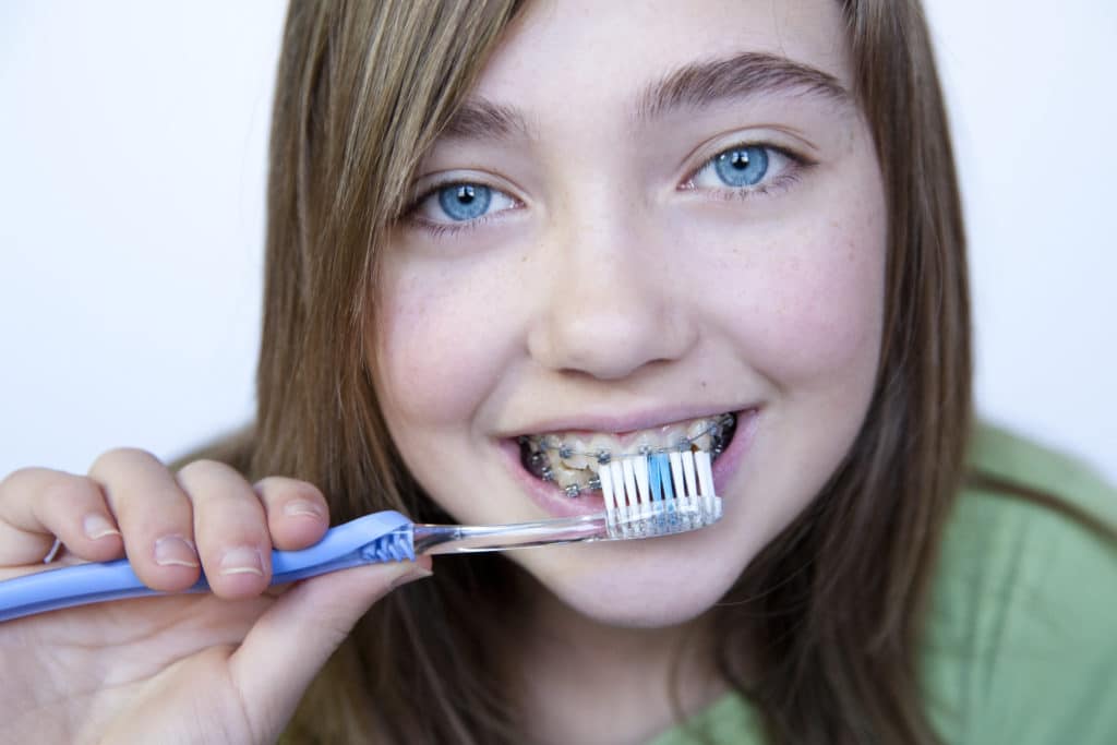face portrait of a teen with braces while brushing her teeth