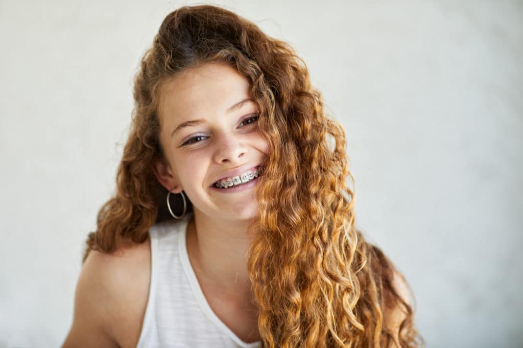 Preteen girl with curly auburn hair, smiling with braces in front of a white background