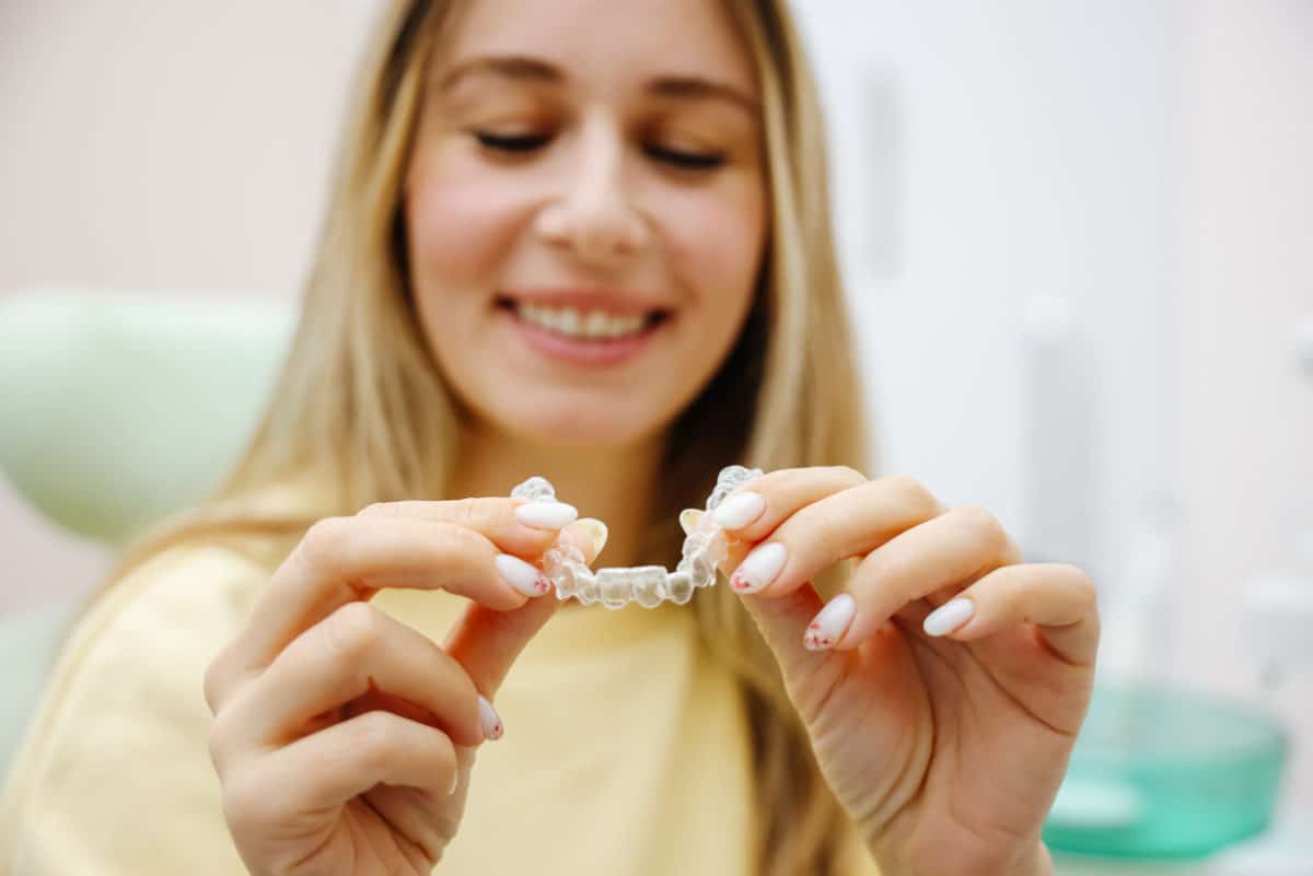 A blonde girl in a yellow t shirt holding up a clear aligner tray