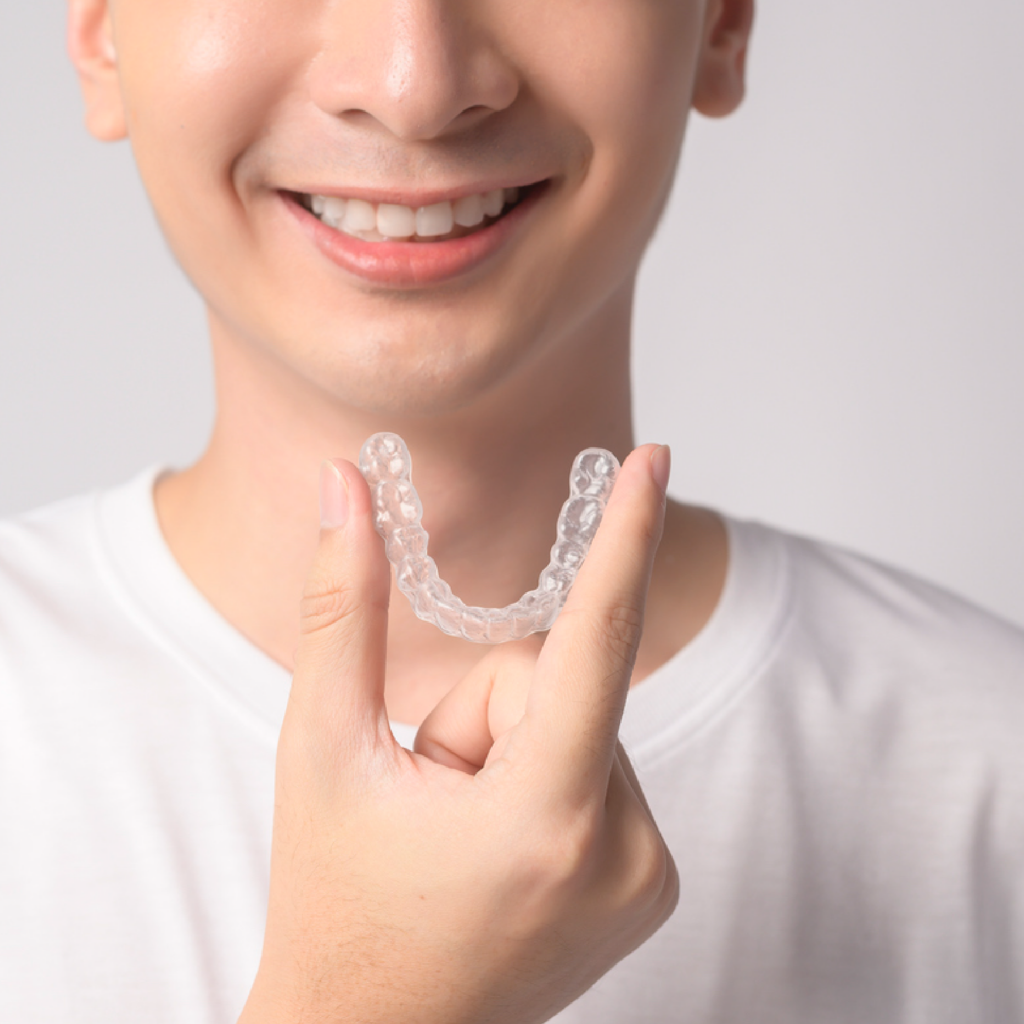 Teen in plain white tee holding his invisalign teen tray between his thumb and index finger