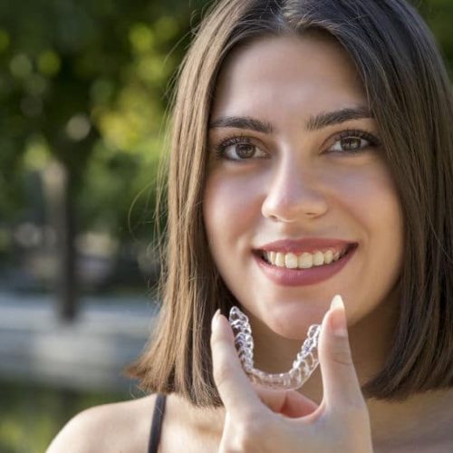 Beautiful smiling Turkish woman is holding an invisalign bracer