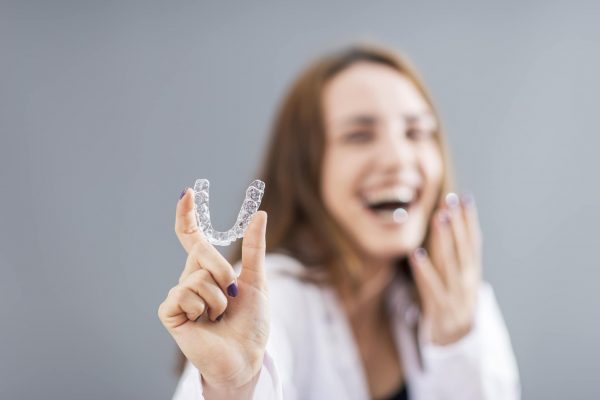 a person smiling while displaying invisalign clear aligners with her fingers