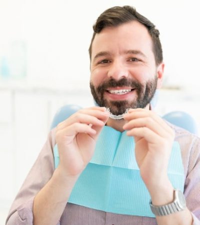Portrait of smiling Caucasian mid adult man holding clear orthodontic retainer