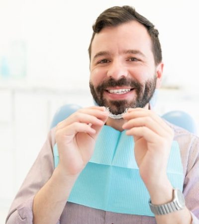 Patient With Invisible Aligner At Clinic Portrait of smiling Caucasian mid adult man holding clear orthodontic retainer