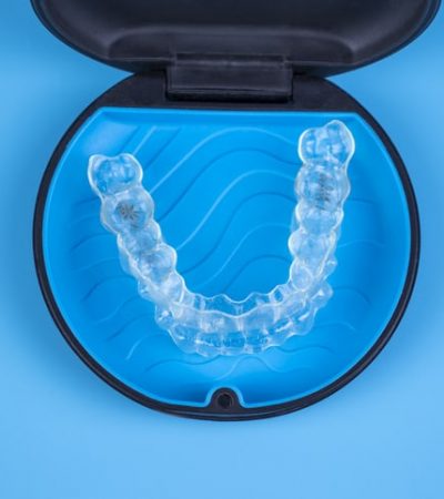 A clear aligner in a blue and black Invisalign tray. The tray is on a blue background.