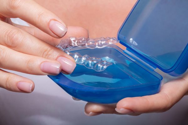 A woman's hand putting a clear aligner back in its storage case.