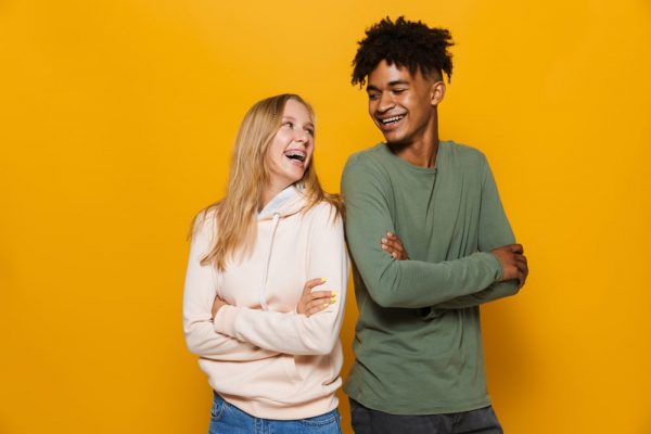 two teens with braces looking at each other and smiling in front of a yellow background