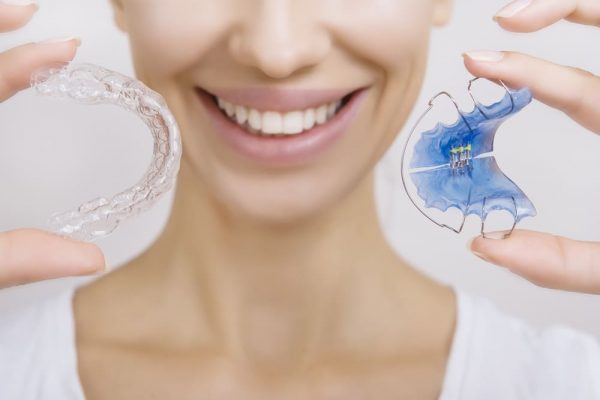 Close up of a woman holding a plastic and wire retainer and a clear aligner tray
